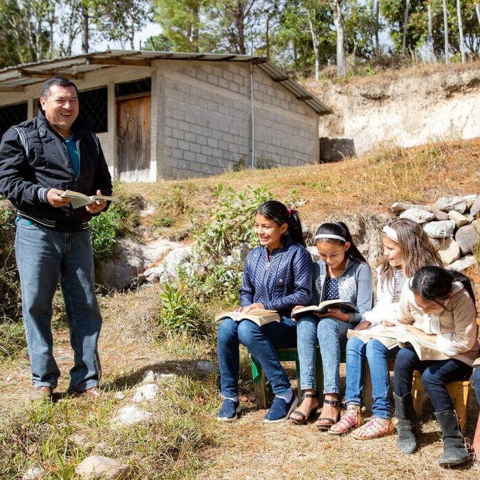 alt="Compassion_20_Jahre_in_Honduras_Kinder_sitzen_auf_einer_Bank_vor_der_Kirchengemeinde"