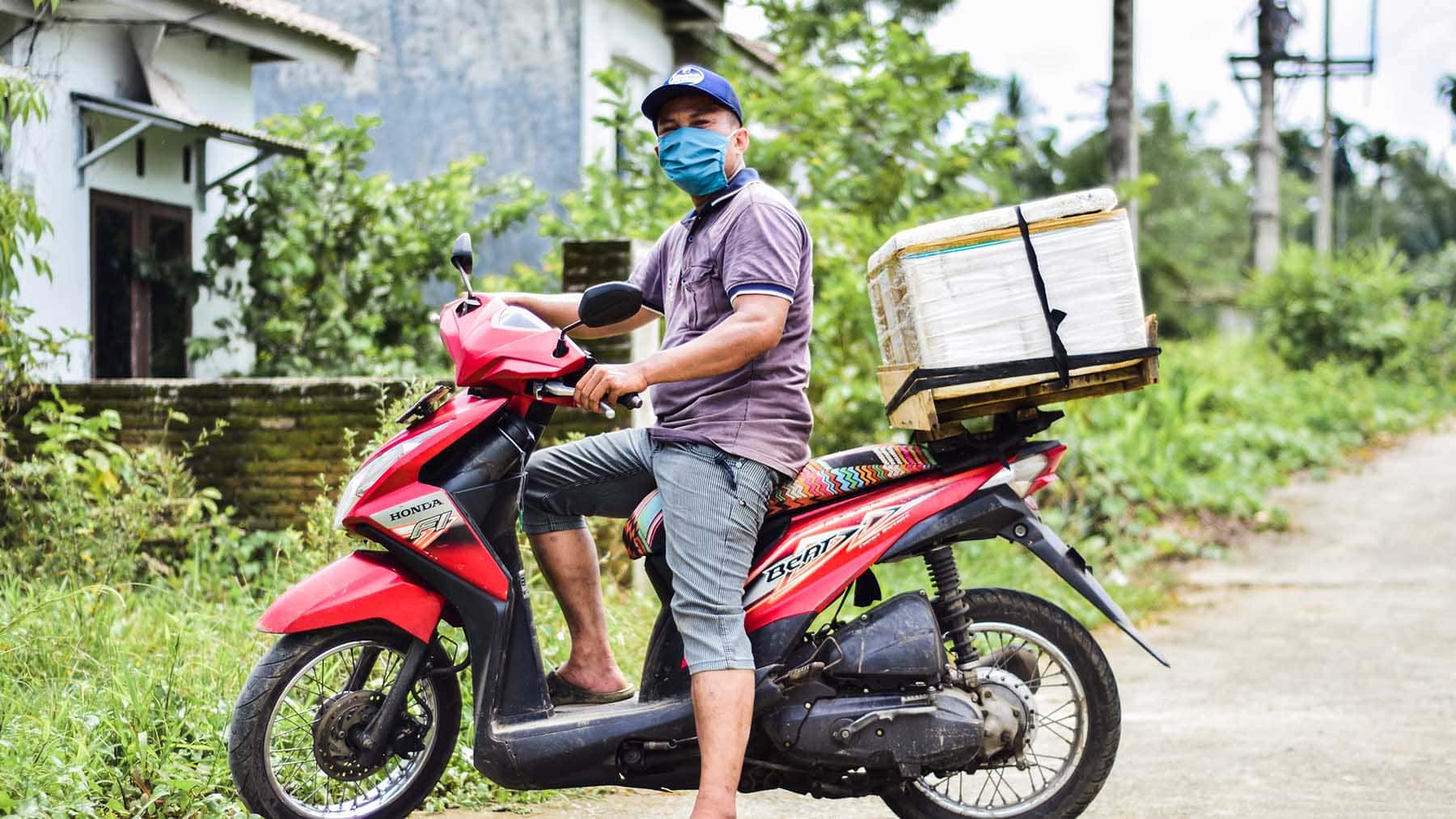 alt="Julius‘ Familie Indonesien Compassion Deutschland 01 Julius auf Motorroller mit Kühlbox"