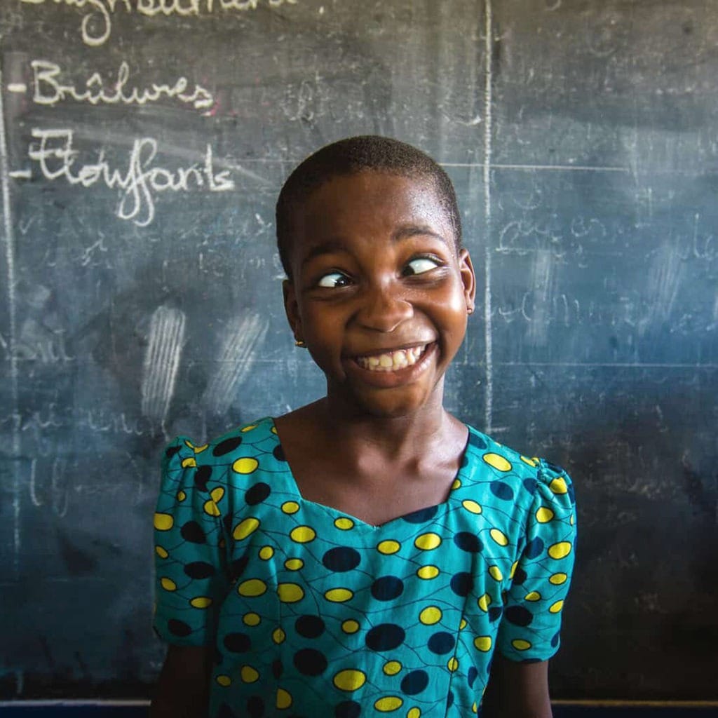 alt="girl-from-togo-in-front-of-a-chalkboard-making-a-funny-face-Compassion-Deutschland"