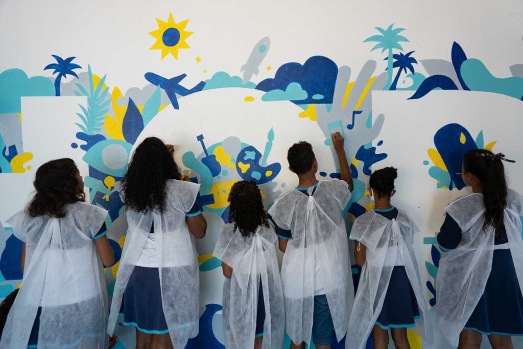 alt="Kinder_gelb_blau_türkis_arthelps_kreativer_workshop_brasilien_stefan_kunz_kinder_bemalen_eine_Wand_im_Compassion_Kinderzentrum"