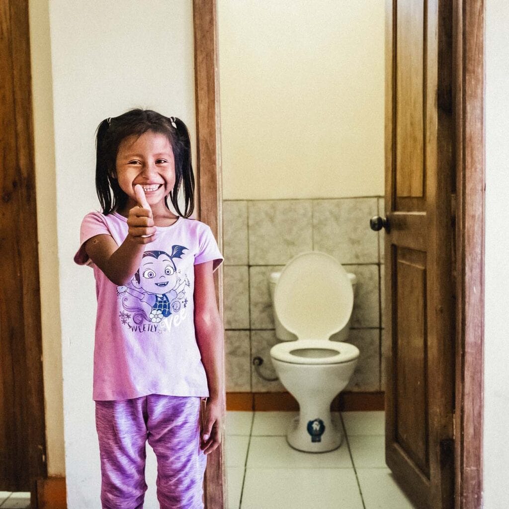 alt="Welttoiletten Tag 2022 Mädchen beim Zähne putzen und Hygiene lernen in einem Toilettenhäuschen in Ecuador