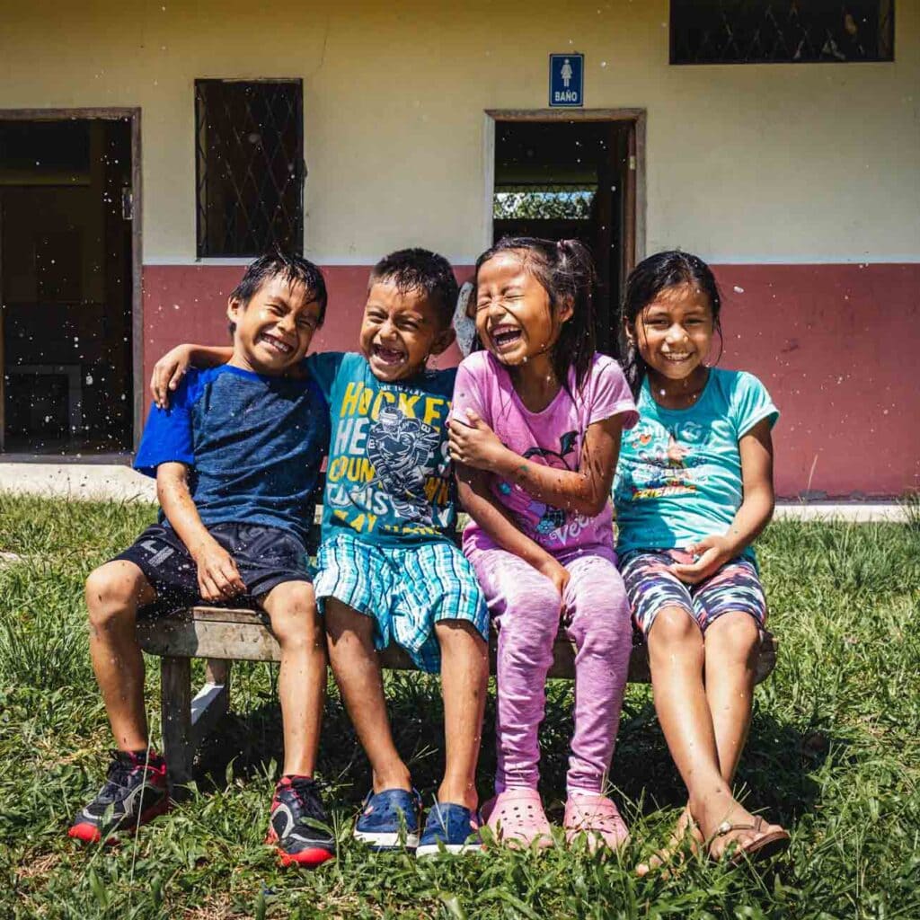 alt="Welttoiletten Tag 2022 Kinder auf einer Bank vor einem Toilettenhäuschen in Ecuador"