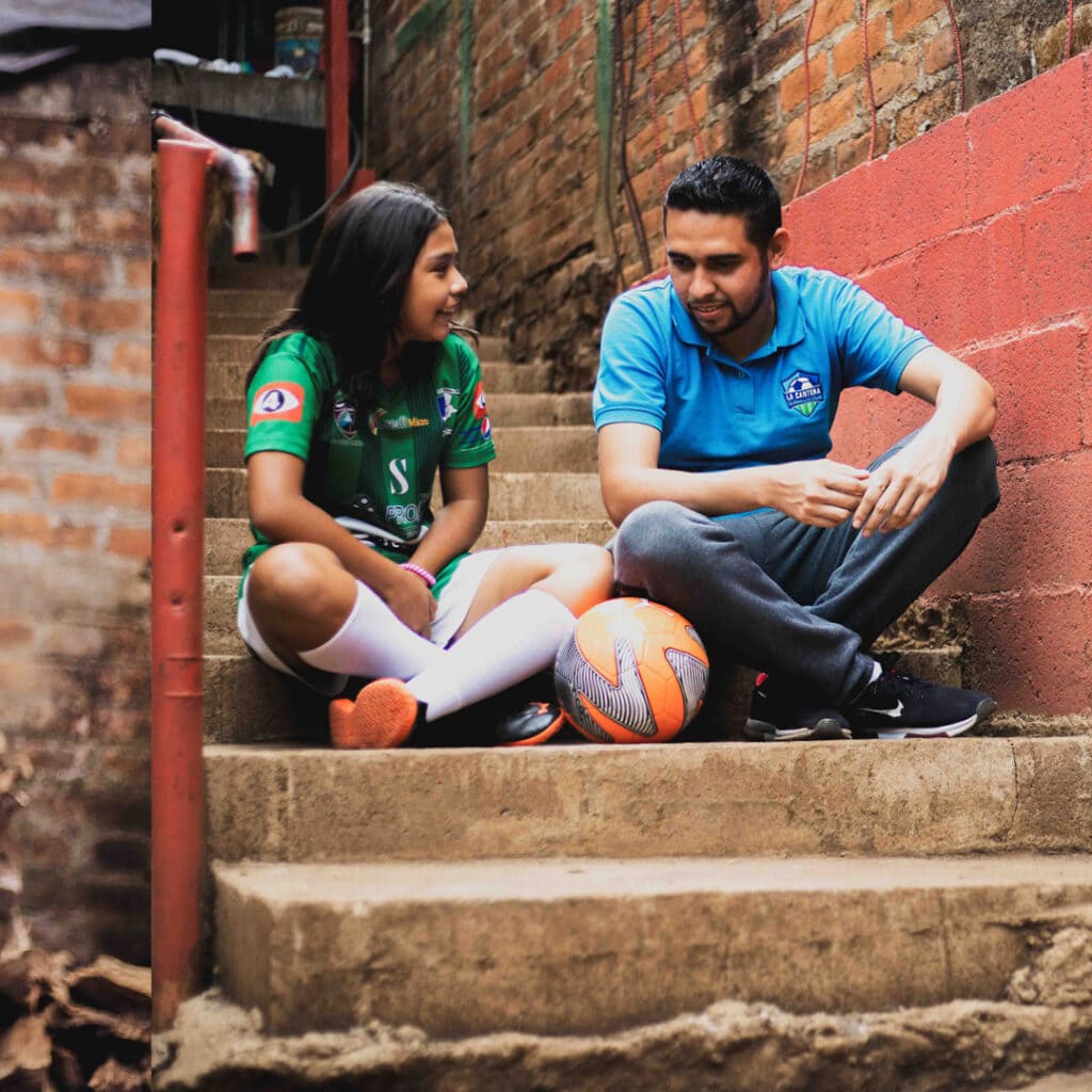 alt="Karlas Geschichte, Fußball spielen ist ihr Hobby, Karla mit ihrem Fußballtrainer, El Salvador"