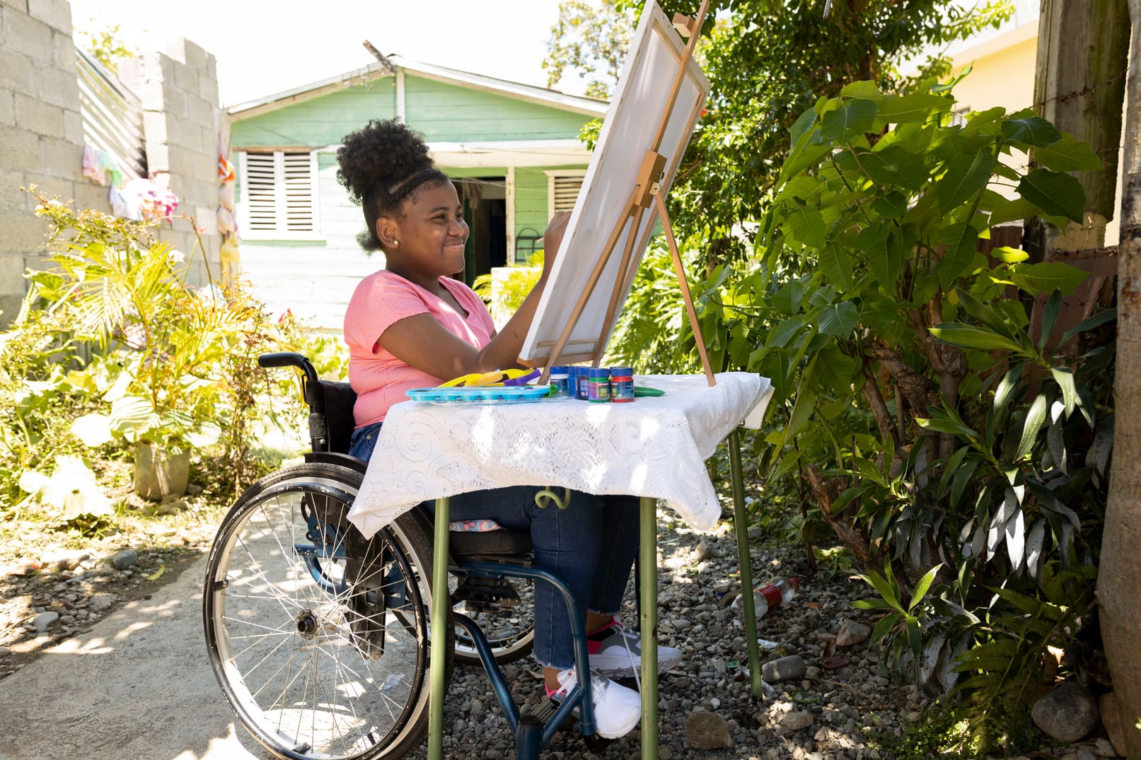 alt="Scarles Geschichte, Dominikanische Republik, ein Mädchen im Rollstuhl am Malen im Garten, Compassion Deutschland"