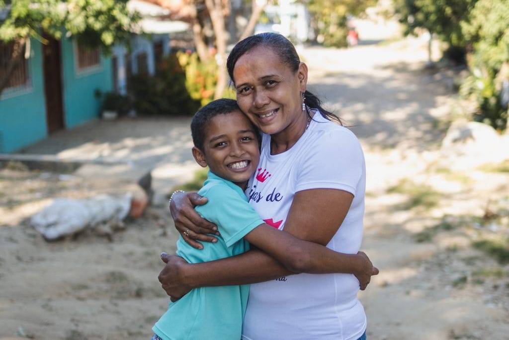 alt="Plastikflaschen werden zu Schmuck, Patricia und Jose umarmen sich, Compassion Deutschland"