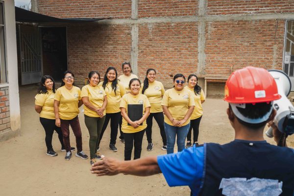 alt="Eine Gruppe von Frauen steht lächelnd vor einem neu errichteten Haus in Peru – Zeichen für Gemeinschaft, Wiederaufbau und Hoffnung nach einer Flutkatastrophe."