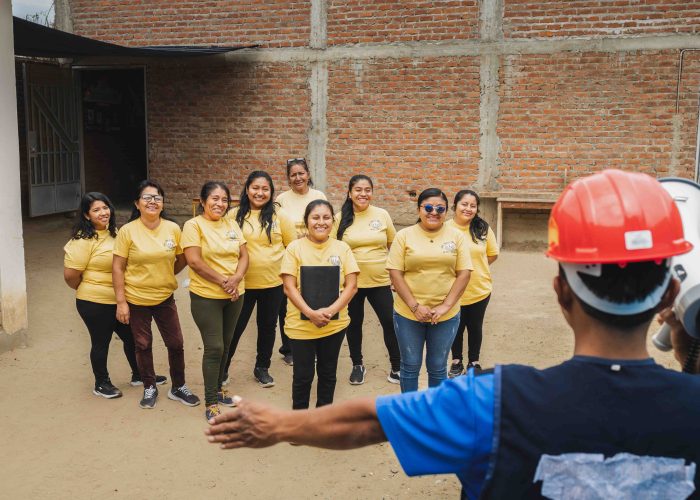 alt="Eine Gruppe von Frauen steht lächelnd vor einem neu errichteten Haus in Peru – Zeichen für Gemeinschaft, Wiederaufbau und Hoffnung nach einer Flutkatastrophe."