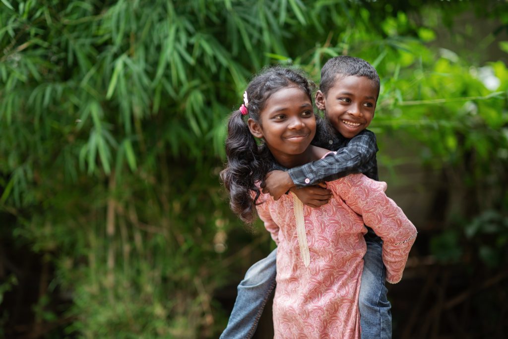 alt="Rita und ihr Bruder, der an ihrem Rücken hängt, in Bangladesch, Compassion Deutschland Patenkind"