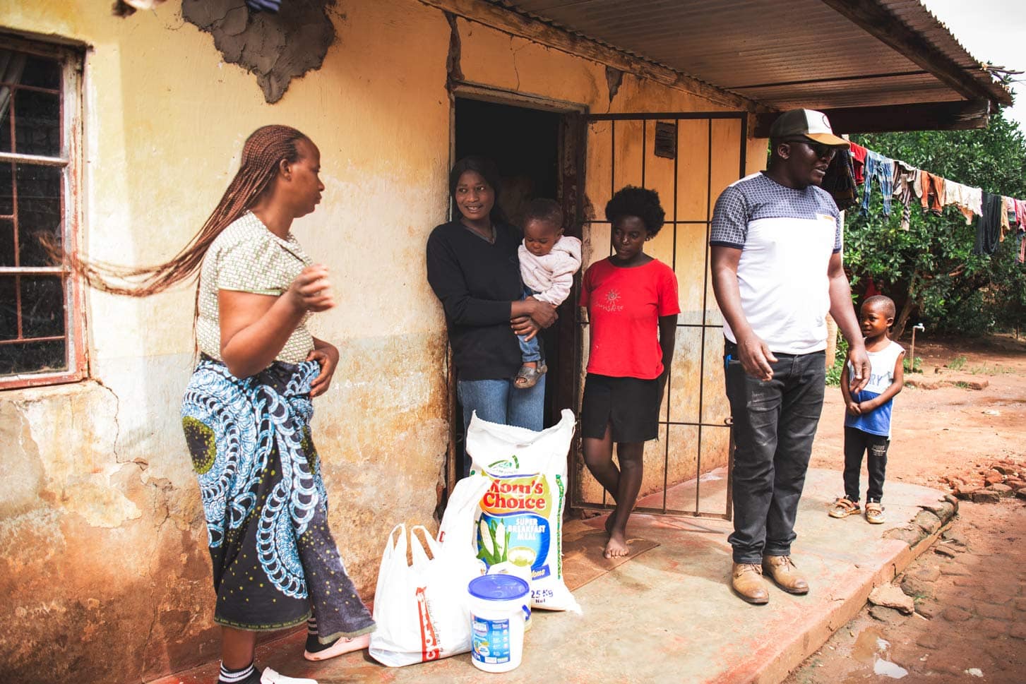 alt="Familien vor einem Haus, Unterstützung durch Compassion Deutschland, nachhaltige Entwicklung, Armut bekämpfen, humanitäre Hilfe."