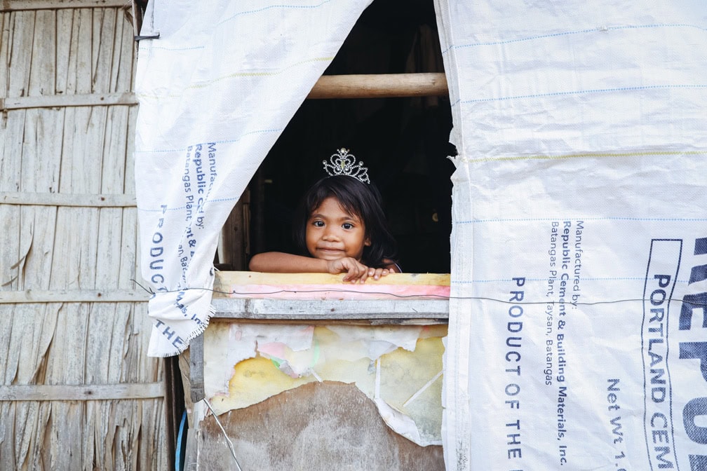 Warum Kinder bei Compassion im Blickpunkt stehen, Kind mit Krone auf dem Kopf lächelt aus einem Fenster, Compassion Deutschland