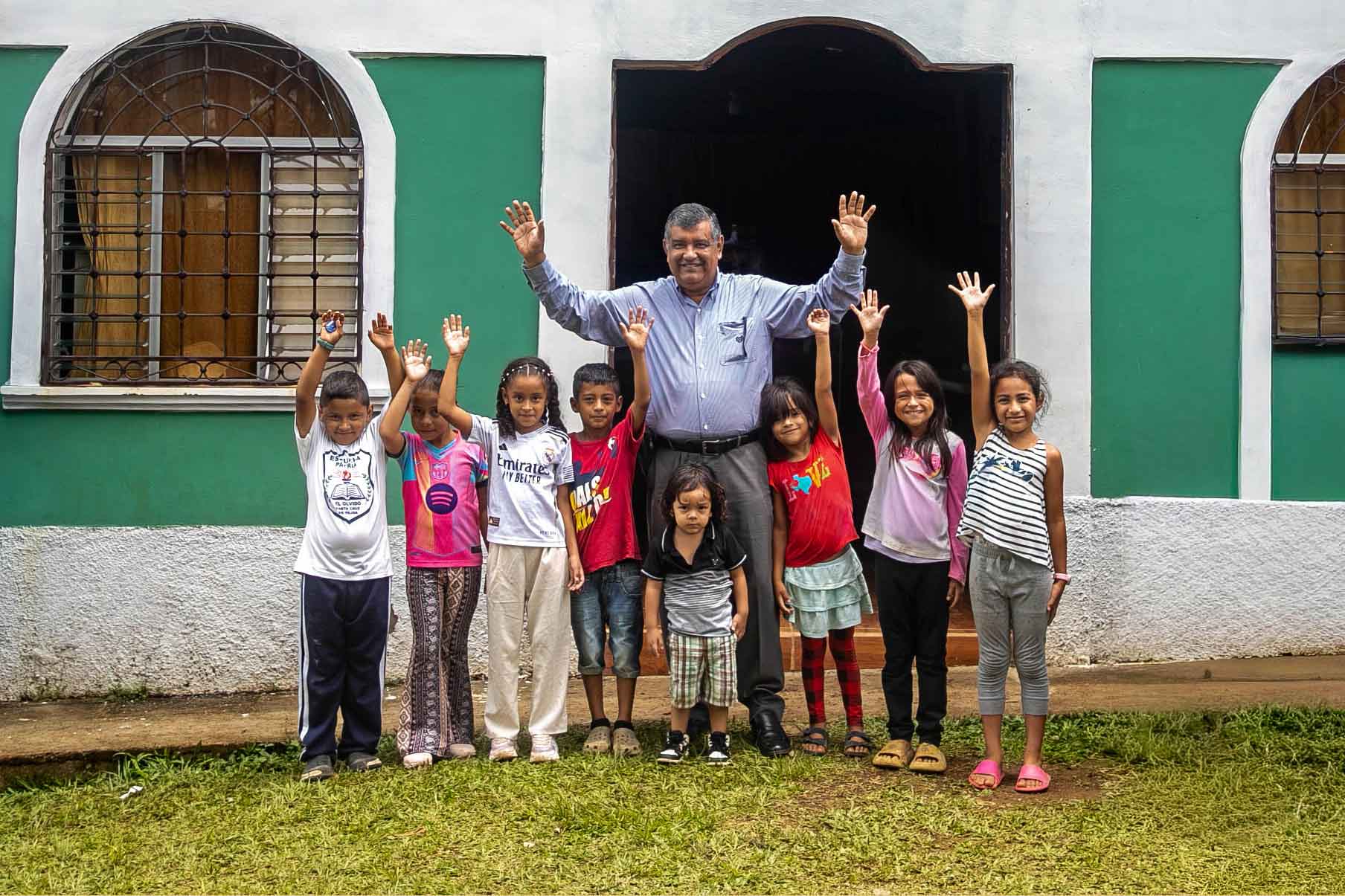 Einsatz für soziale Gerechtigkeit in Honduras, Pastor winkt mit Kids aus Kinderzentrum in die Kamera, Compassion Deutschland