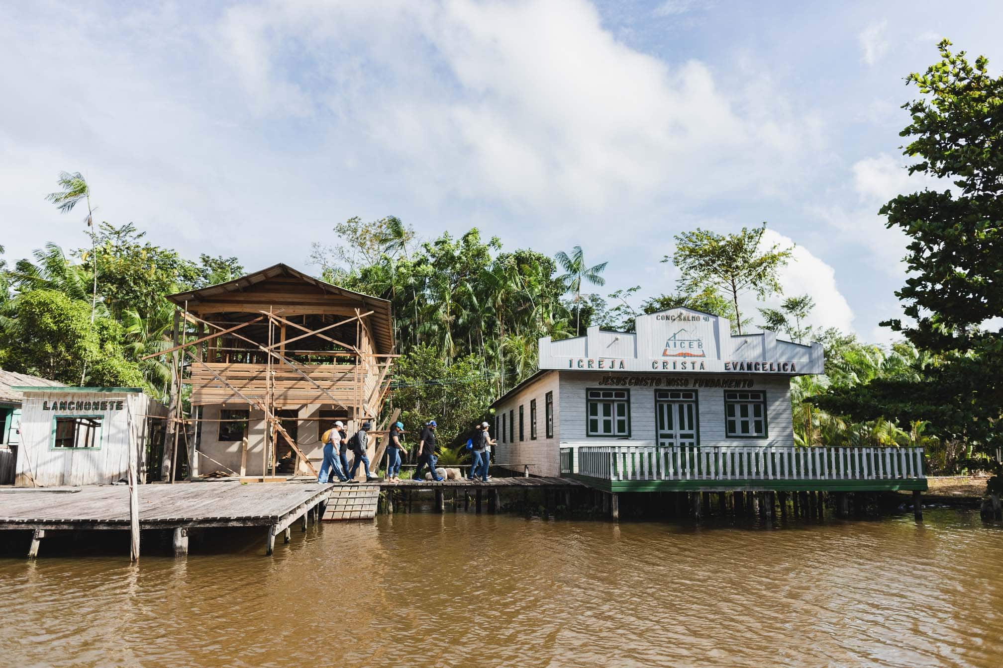 alt="Bauarbeiter laufen über einen Steg und bauen ein neues Haus aus Holz auf der Marajó-Insel am Amazonas, Compassion Deutschland"